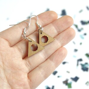 May include: A pair of wooden triangle earrings with a circular cutout in the center. The earrings are on a silver hook.