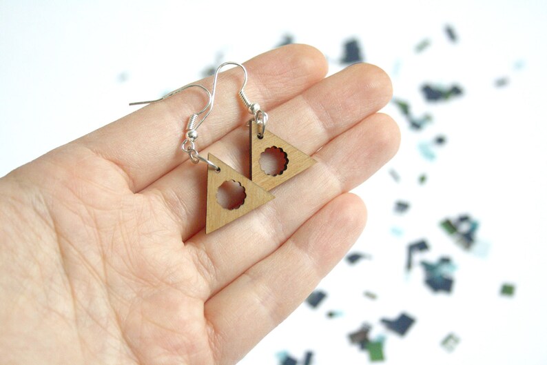 May include: A pair of wooden triangle earrings with a circular cutout in the center. The earrings are on a silver hook.