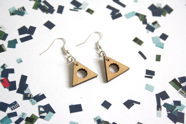May include: A pair of wooden triangle earrings with a circle cutout in the center. The earrings are a light brown color and have silver hooks.