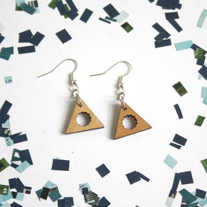 May include: A pair of wooden triangle earrings with a circle cutout in the center. The earrings are a light brown color and have silver hooks.