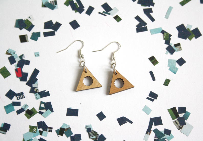 May include: A pair of wooden triangle earrings with a circle cutout in the center. The earrings are a light brown color and have silver hooks.