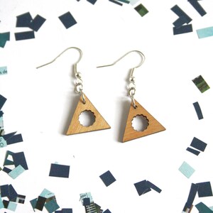 May include: A pair of wooden triangle earrings with a circle cutout. The earrings are light brown and have silver hooks.