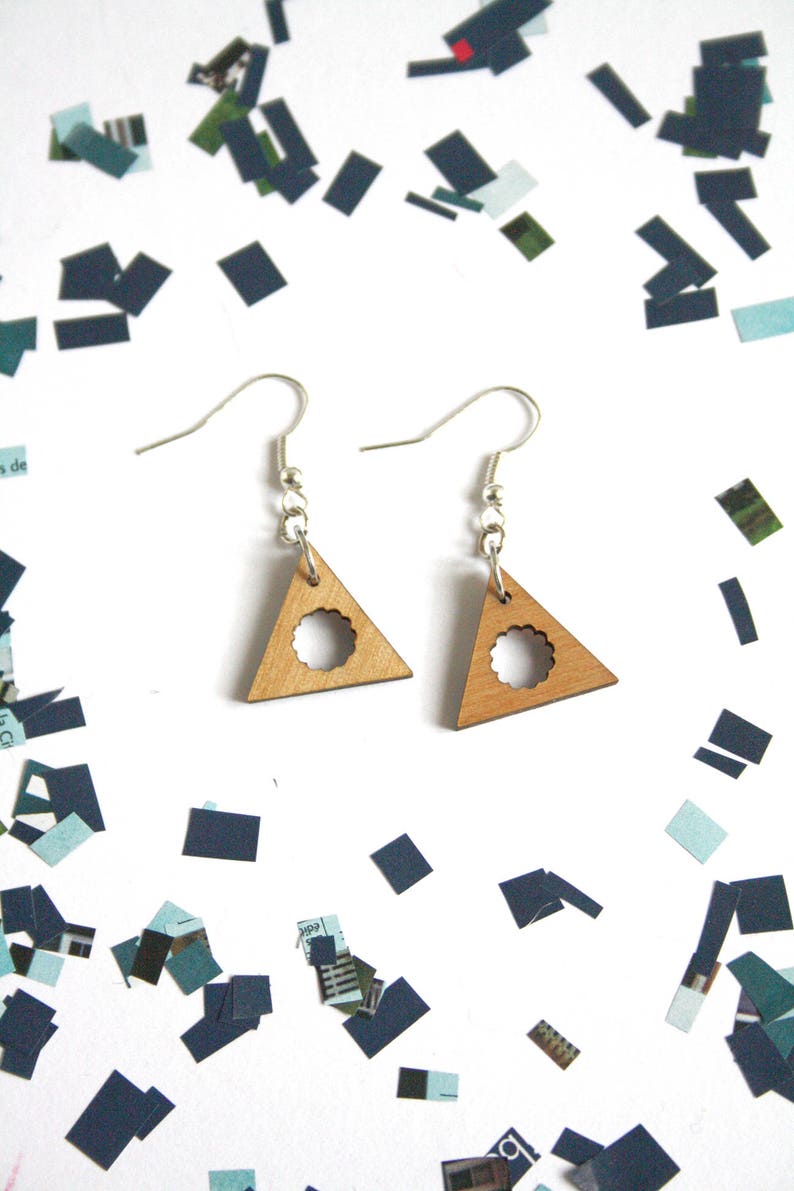 May include: A pair of wooden triangle earrings with a circle cutout. The earrings are light brown and have silver hooks.