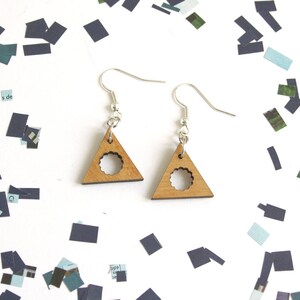 May include: A pair of wooden earrings shaped like triangles with a circle cut out of the center. The earrings are silver and have a simple design.