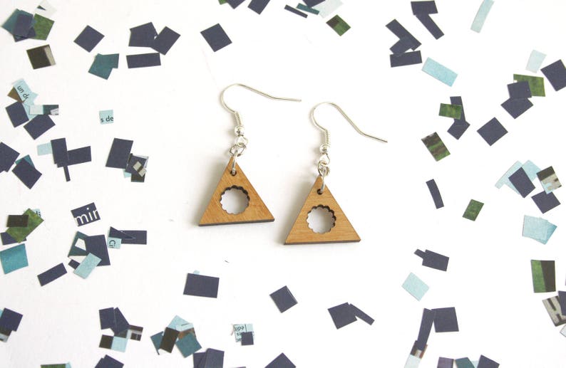 May include: A pair of wooden earrings shaped like triangles with a circle cut out of the center. The earrings are silver and have a simple design.