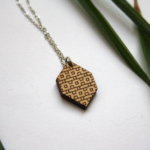 May include: A wooden pendant necklace with a geometric pattern. The pendant is a light brown color and has a silver chain.