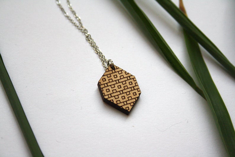 May include: A wooden pendant necklace with a geometric pattern. The pendant is a light brown color and has a silver chain.