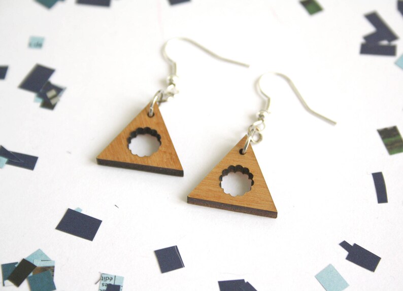 May include: A pair of wooden triangle earrings with a circle cutout. The earrings are light brown with a darker brown edge and have silver hooks.
