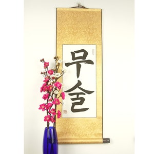 May include: A traditional Japanese scroll with gold accents and black calligraphy that reads "Early Spring". The scroll is hanging on a white wall with a vase of pink and white flowers in front of it.