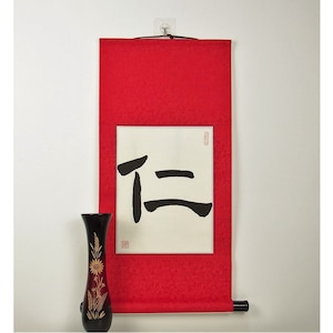 Könnte beinhalten: Eine rote Schriftrolle mit einem schwarzen chinesischen Kalligraphiezeichen auf weißem Hintergrund. Das Zeichen ist "正" und bedeutet "richtig" oder "aufrecht".