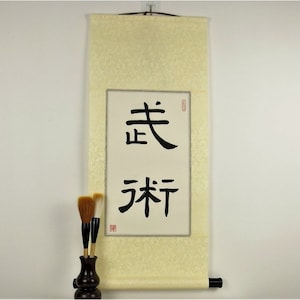 May include: A cream-colored scroll with black Chinese calligraphy that reads "美" and "祈". The scroll is mounted on a wooden dowel and has a red seal.