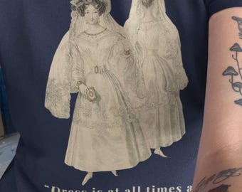 Puede incluir: Camiseta azul marino con una ilustración vintage de dos mujeres con vestidos y velos blancos. La cita "Dress is at all times a frivolous distinction." de Jane Austen está impresa debajo.