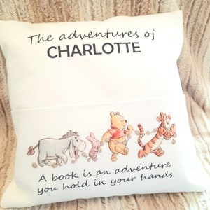 May include: White pillow with a Winnie the Pooh and friends design. The text on the pillow reads "The adventures of CHARLOTTE A book is an adventure you hold in your hands".