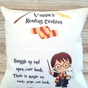 May include: White reading cushion with a Harry Potter theme. It features a cartoon image of Harry Potter holding his wand and Hedwig the owl. The text on the cushion reads "Vinnie's Reading Cushion" and "Snuggle up and open your book, There is magic on every page you look."