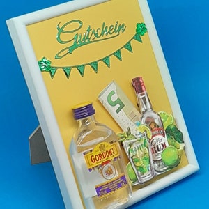 Könnte beinhalten: Ein gelber Bilderrahmen mit einem grün-weißen Banner, auf dem "Gutschein" steht. Das Bild zeigt eine Miniaturflasche Gordon's Gin, eine Flasche Old Rum, ein Glas Mojito und ein paar Geldscheine.