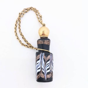May include: A black glass bottle with a gold top and a white and gold design. The bottle is attached to a gold chain.