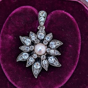 May include: A silver pendant with a pearl in the center and a starburst design of clear stones.
