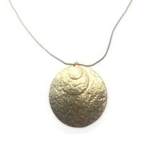 May include: A gold necklace featuring a layered circle pendant. The pendant is made of two overlapping circles, both with a hammered texture.