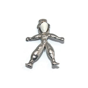 Puede incluir: Un pin de tono plateado con forma de persona que lleva un traje espacial. La cabeza de la persona es un óvalo blanco.