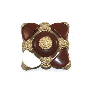 May include: A brown and white geometric brooch with gold accents. The brooch features a central circle with a smaller circle inside, surrounded by four curved shapes.