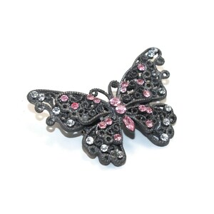 Può includere: Un fermaglio a forma di farfalla in metallo nero con strass rosa e trasparenti.