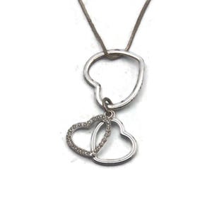 May include: Silver necklace with two interlocking heart pendants. The smaller heart is encrusted with clear rhinestones.