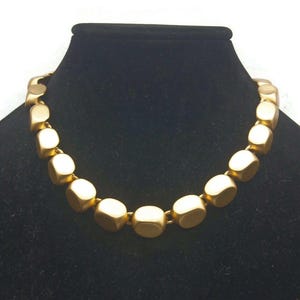 May include: A gold necklace made of large, square-shaped beads.