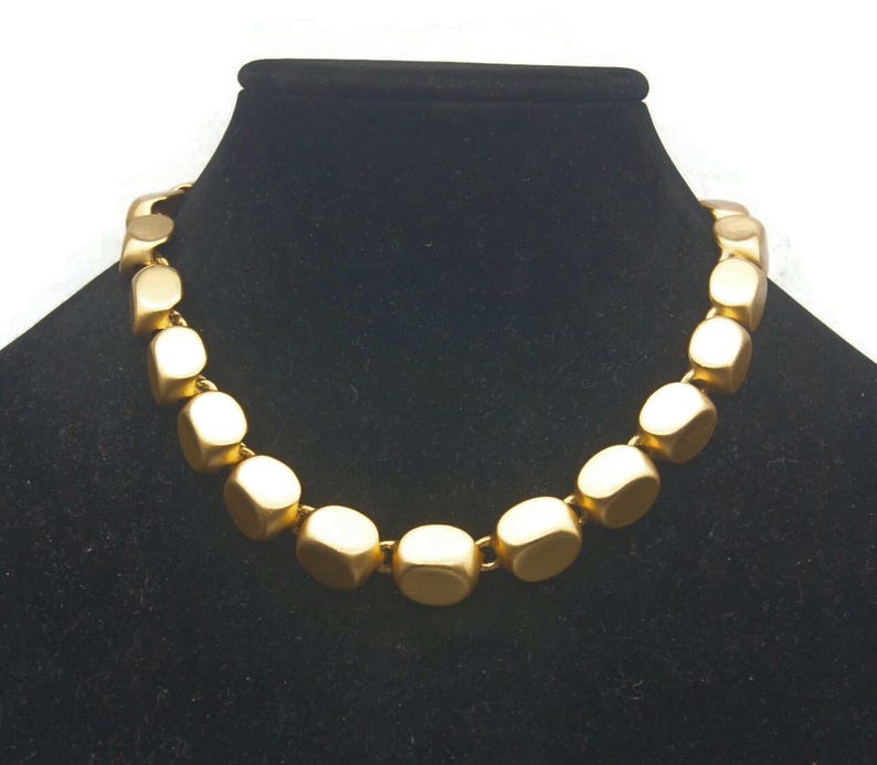 May include: A gold necklace made of large, square-shaped beads.