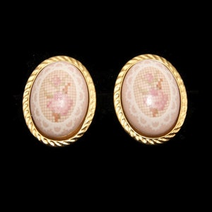May include: A pair of gold oval-shaped earrings with a white and pink floral design.