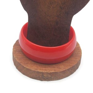 Op de afbeelding: Een felrode plastic armband op een houten standaard.