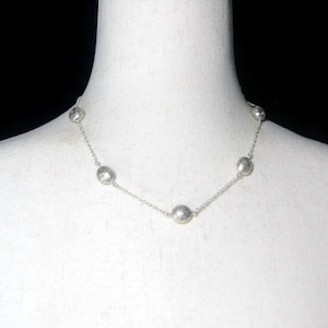 May include: A silver necklace with six textured, round beads evenly spaced along a delicate chain. The beads have a detailed, patterned surface. The necklace is displayed on a white mannequin.