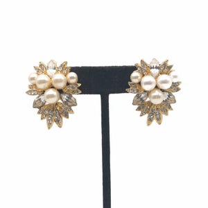 May include: A pair of gold tone earrings with a cluster of faux pearls and clear rhinestones.