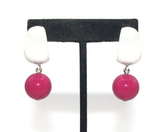 May include: A pair of white and pink dangle earrings. The earrings feature a white, curved, geometric shape with a pink ball hanging from it.