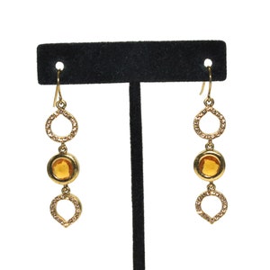 Op de afbeelding: Gouden oorhangers met een traanvormige hanger, een ronde amberkleurige steen en een cirkelhanger.