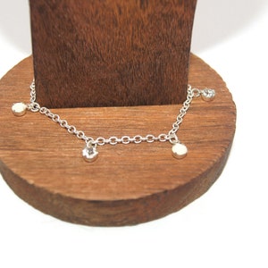 May include: A silver chain anklet with three small round charms. The charms are silver with a clear crystal center.