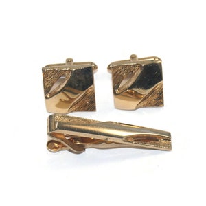 May include: A set of gold-toned cufflinks and a tie clip. The cufflinks and tie clip have a geometric design.