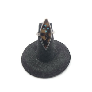 May include: A silver ring with a brown and black stone set in a diamond shape. The stone has turquoise accents.