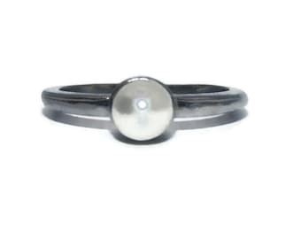 May include: A silver ring with a white pearl-like centre stone.