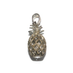 May include: A silver pineapple charm with a gold-toned finish. The charm is detailed with a textured pineapple design and a loop for attaching to a necklace or bracelet.