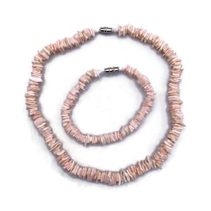May include: A necklace and bracelet set made from small, pale pink shell chips. The necklace and bracelet have a matching design and are connected with silver clasps. The jewellery is displayed against a white background.