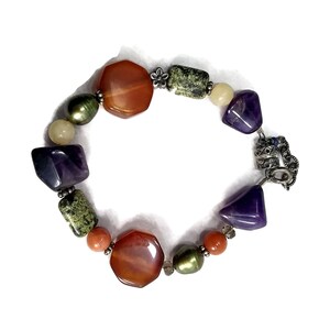 May include: A multi-colored gemstone bracelet with a silver clasp. The bracelet features orange, green, purple, and white stones.