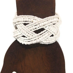 May include: White beaded bracelet with a woven design. The bracelet is made of many strands of small white beads.