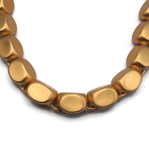 May include: A gold necklace with large, oval-shaped beads. The beads are matte and have a slightly textured surface.