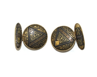 May include: A pair of gold cufflinks with black and gold geometric designs. The cufflinks are round with a raised design.