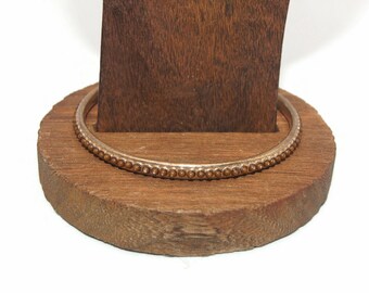 May include: A silver bangle bracelet with a row of small brown beads around the edge. The bracelet is displayed on a wooden stand.