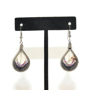 May include: A pair of silver teardrop earrings with a woven design in shades of white, black, and iridescent colors.