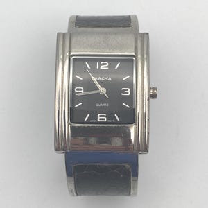 May include: A rectangular Magna quartz watch with a black face and silver-tone metal casing. The watch has a black leather band and displays the time with white numerals. The watch face reads "Magna" and "Quartz".