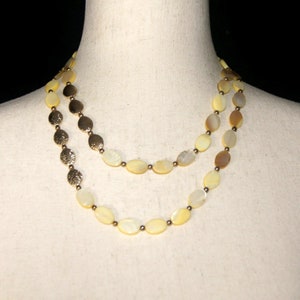 May include: A double strand necklace made of oval-shaped, iridescent, light yellow shell beads with gold accents.