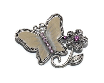 May include: A silver butterfly brooch with a pearl-like finish and purple rhinestones. The butterfly is attached to a silver flower with a purple rhinestone center.