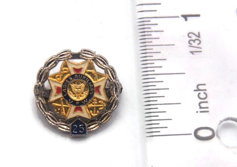 K&ouml;nnte beinhalten: Eine Vintage-Anstecknadel der Ladies Auxiliary VFW. Die Anstecknadel ist rund, mit einem zentralen Emblem mit einem Adler und dem Text "Ladies Auxiliary VFW". Sie hat ein wei&szlig;es, rotes und goldenes Sternmuster, umgeben von einem silbernen Kranz und der Zahl "25".